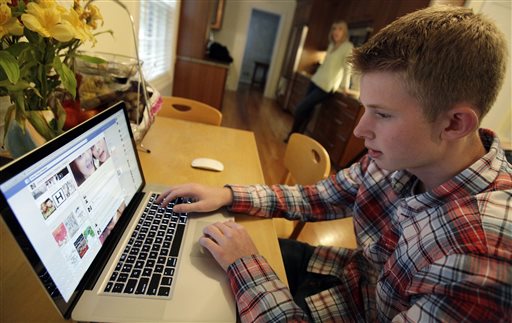 In this Oct. 24, 2013 photo, Mark Risinger, 16, checks his Facebook page on his computer as his mother, Amy Risinger, looks on at their home in Glenview, Ill. The recommendations are bound to prompt eye-rolling and LOLs from many teens but an influential pediatrician's group says unrestricted media use has been linked with violence, cyber-bullying, school woes, obesity, lack of sleep and a host of other problems. Marks mom said she agrees with restricting kids time on social media but that deciding on other media limits should be up to parents. (AP Photo/Nam Y. Huh)