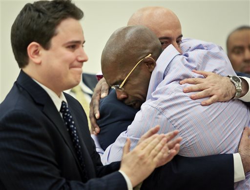 Jonathan Fleming, hugs his attorney Anthony Mayol while his other attorney Taylor Koss applaud in Brooklyn's Supreme court, after a judge declared him a free man on Tuesday April 8, 2014 in New York.  Fleming, who spent almost a quarter-century behind bars for murder, was cleared of a killing that happened when he was 1,100 miles away on a Disney World vacation in 1989. (AP Photo/Bebeto Matthews)