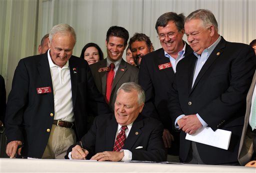 Surrounded by bill supporters, Georgia Gov. Nathan Deal signs House Bill 60 into law during a signing event Wednesday, April 23, 2013, in Ellijay, Ga. The bill makes several changes to the state's gun law. It allows those with a license to carry to bring a gun into a bar without restriction and into some government buildings that don't have certain security measures. It also allows religious leaders to decide whether it's OK for a person with a carry license to bring a gun into their place of worship. (AP Photo/Atlanta Journal-Constitution, Brant Sanderlin)