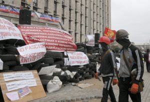 Masked pro-Russian activists pass by a barricade as they guard a regional administration building that they had seized earlier in Donetsk, Ukraine, Friday, April 11, 2014. (AP Photo/Efrem Lukatsky)
