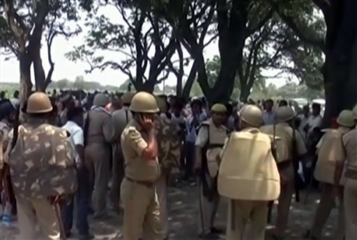 In this Wednesday, May 28, 2014 image taken from video, police stand amongst the crowd near where two teenage sisters were found hanging from a mango tree in the Katra village in Uttar Pradesh state, in northern India. Authorities have arrested three men, including two police officers, suspected of gang-raping and killing the teenagers before hanging their bodies from the tree, sparking renewed public outrage over sexual violence in the country. (AP Photo/NNIS via AP Video)