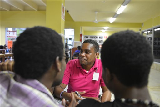 In this, April 25, 2014, photo, gay rights activist James Burton, center, of the Color Pink Group, chats with a group of young homosexual men about HIV and health issues at a shopping mall in Kingston, Jamaica. Gay sex and prostitution is illegal in Jamaica, and LGBT people who sell sex face arrest or worse. But this normally wary group is welcoming a recent outreach as a volunteer reaches out to tthem with health advice. (AP Photo/David McFadden)