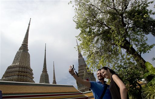 A couple of Western tourists snap a souvenir photo at a Wat Pho temple in Bangkok, Thailand Tuesday, May 27, 2014. The drama of Thailand's military takeover has played out mainly in the political arena. While the army detains political leaders and issues stern warnings on TV, tourists are kicking back on the countrys famed beaches and sightseeing in Bangkok. The main impact on visitors for now is a 10 p.m. curfew, which forces nightlife to close four hours earlier. (AP Photo/Sakchai Lalit)