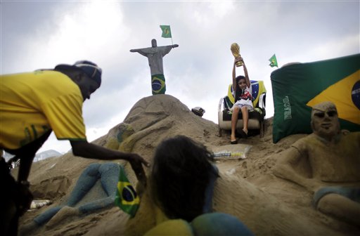 A young girl lifts a replica of the World Cup trophy next to a sand sculpture of Rio de Janeiro's iconic Christ the Redeemer along the Copacabana beach, Wednesday, June 11, 2014 in Rio de Janeiro, Brazil. The World Cup 2014 tournament will be held in Brazil and starts on June 12. (AP Photo/Wong Maye-E)