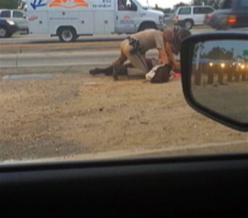 In this July 1, 2014 image made from video provided by motorist David Diaz, a California Highway Patrol officer, left, aided by another man, stand over a woman while punching her in the head on the shoulder of a Los Angeles freeway. The woman had been walking on Interstate 10 west of downtown Los Angeles, endangering herself and people in traffic, and the officer was trying to restrain her, CHP Assistant Chief Chris O'Quinn said at a news conference. The officer, who has not been identified, has been placed on administrative leave during an investigation. (AP Photo/David Diaz)