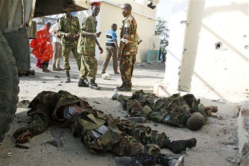GRAPHIC CONTENT - Somali government soldiers look at the dead bodies of al-Shabab militants on a road near the main gate of the presidential palace in Mogadishu, Somalia, Wednesday, July, 9, 2014. Somali troops retook the presidential palace in the capital of Mogadishu after militants forced their way in and exchanged heavy gunfire with troops and guards Tuesday, the latest attack underscoring the threat posed by Islamic extremist group al-Shabab in east Africa.  (AP Photo/Farah Abdi Warsameh)