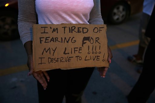 A demonstrator holds a sign Thursday, Aug. 14, 2014, in Ferguson, Mo.  Hundreds of people protesting the death of  Michael Brown marched through the streets of Ferguson alongside state troopers Thursday. (AP Photo/Jeff Roberson)