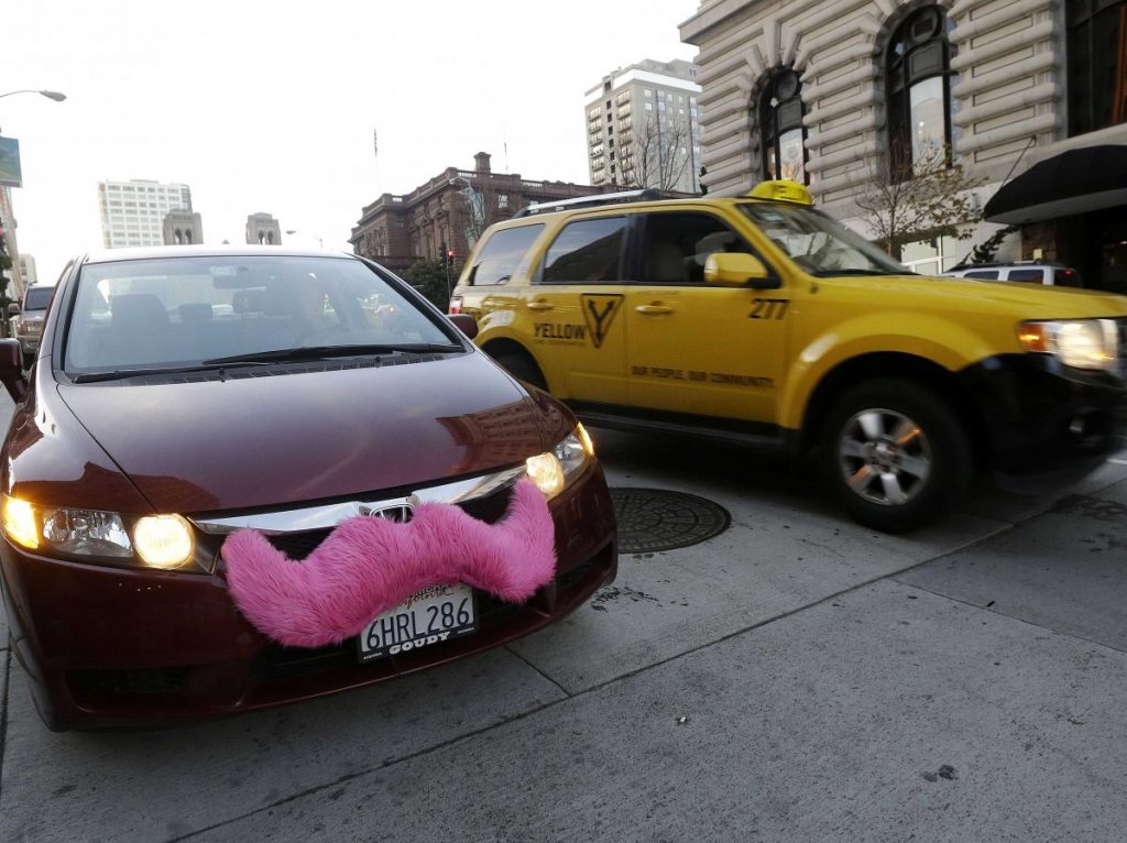 A Lyft car with its trademark pink moustache next to a yellow taxi in San Francisco. (AP Photo)