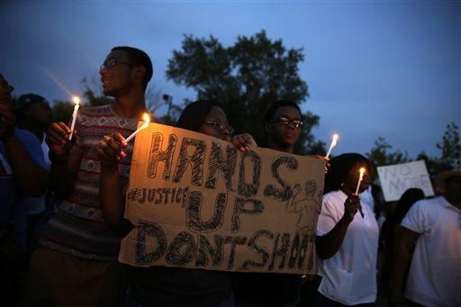 Demonstrators hold candles and signs Thursday, Aug. 14, 2014, in Ferguson, Mo. Hundreds of people protesting the death of  Michael Brown marched through the streets of Ferguson alongside state troopers Thursday. (AP Photo/Jeff Roberson)
