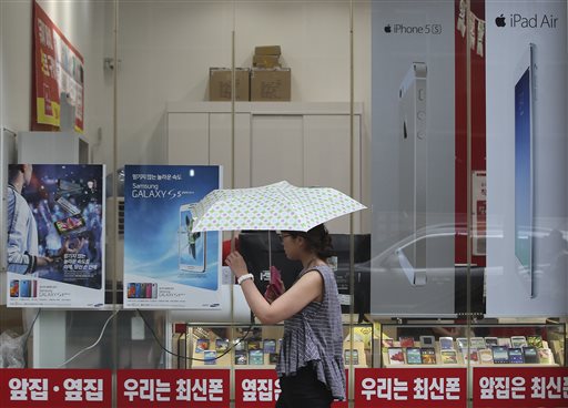 A woman walks by advertisement posters of Samsung Electronics' Galaxy S5, Apple's iPhone 5s and iPad Air at a mobile phone shop in Seoul, South Korea, Wednesday, Aug. 6, 2014. Samsung and Apple Inc. have agreed to end all patent lawsuits between each other outside the U.S. in a step back from three years of legal hostilities between the world's two largest smartphone makers. (AP Photo/Ahn Young-joon)