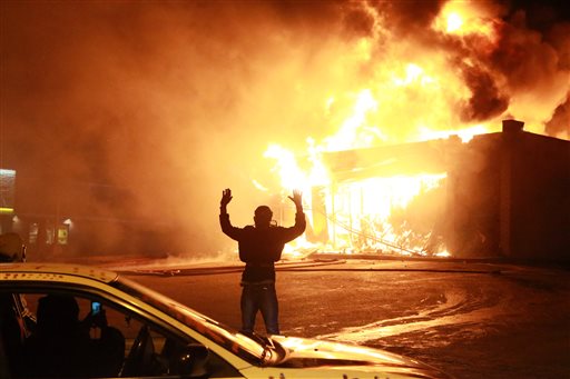 In this Nov. 24, 2014 photo, a protestor poses for a "hands up" photo in front of a burning building on West Florissant Ave. in Ferguson, Mo. Hands Up, Dont Shoot has become a rallying cry despite questions whether Michael Browns hands were raised in surrender before being fatally shot by a Ferguson police officer. (AP Photo/St. Louis Post-Dispatch, Christian Gooden, File)