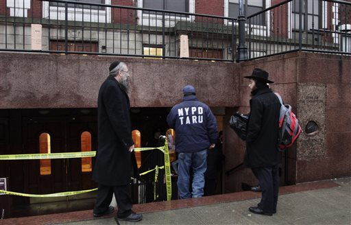Members of the Lubavitch community watch a police officer enter Chabad-Lubavitch Hasidic headquarters, Tuesday, Dec. 9, 2014, in New York.  A knife-wielding man stabbed an Israeli student inside the Brooklyn synagogue before being fatally shot by police after he refused to drop the knife. The student, Levi Rosenblatt, is in stable condition. (AP Photo/Mark Lennihan)