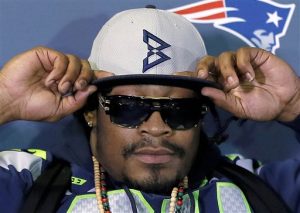Seattle Seahawks' Marshawn Lynch adjusts his cap during an interview for the NFL Super Bowl XLIX football game, Thursday, Jan. 29, 2015, in Phoenix. The NFL may not like those "Beast Mode" caps Lynch has been wearing during his Super Bowl press appearances, but the fans apparently do. As the league reportedly considers fining Lynch for promoting an unauthorized brand, the New Era Cap Co. is busy making more of the caps after they sold out on Lynch's website. (AP Photo/Matt York)