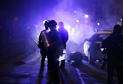 In this Nov. 25, 2014 file photo, police officers watch protesters as smoke fills the streets in Ferguson, Mo. after a grand jury's decision in the fatal shooting of Michael Brown. Six months after 18-year-old Michael Brown died in the street in Ferguson, Missouri, the Justice Department is close to announcing its findings in the racially charged police shooting that launched "hands up, don't shoot" protests across the nation. (AP Photo/Charlie Riedel, File)