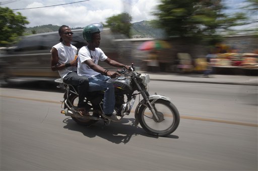 In this May 21, 2015 photo, Joseph Marc Carel, a motorcycle taxi driver, takes a passenger to downtown Port-au-Prince, Haiti. Carel knows the danger of ferrying passengers on his small motorbike, sometimes two at a time, as tides of the buzzing vehicles cut through the chaotic Haitian capital. He has a prosthetic leg to prove it. (AP Photo/Dieu Nalio Chery)