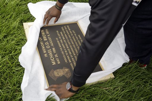 Michael Brown Sr. unwraps a plaque remembering his son, Michael Brown, to show volunteers as they remove items left at a makeshift memorial to Michael Brown Wednesday, May 20, 2015, in Ferguson, Mo. The memorial that has marked the place where Brown was fatally shot by a police officer in August has been removed and will be replaced with a permanent plaque. (AP Photo/Jeff Roberson)