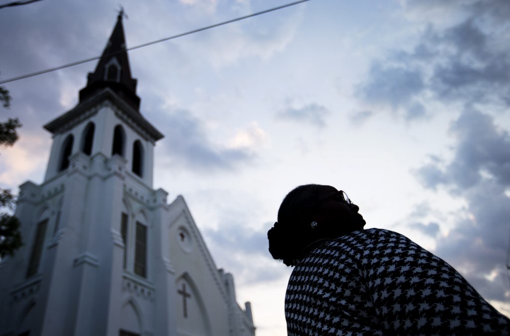 Doris Simmons, of Charleston, S.C. stands next to Emanuel AME Church, the scene of last week's mass shooting, as the sun rises Friday, June 26, 2015, in Charleston.  President Barack Obama delivered the eulogy for one of the victims, Sen. Clementa Pinckney, during his funeral Friday at a nearby college arena. (AP Photo/David Goldman)