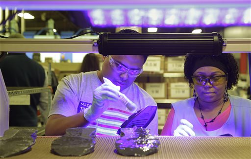 In this photo taken Wednesday July 1, 2015, workers, under ultraviolet light, apply cement to the midsole of the military tested New Balance 950v2 sneaker before the outsole is attached in Boston. New Balance is pressing the Pentagon to buy American-made footwear for the troops instead of sneakers from rival Nike that are made in China. (AP Photo/Stephan Savoia)