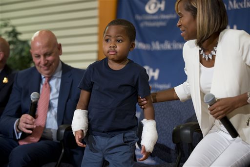 Double-hand transplant recipient eight-year-old Zion Harvey accompanied by Dr. L. Scott Levin, left, and his mother Pattie Ray, stands during a news conference Tuesday, July 28, 2015, at The Childrens Hospital of Philadelphia (CHOP) in Philadelphia. Surgeons said Harvey of Baltimore who lost his limbs to a serious infection,  has become the youngest patient to receive a double-hand transplant. (AP Photo/Matt Rourke)