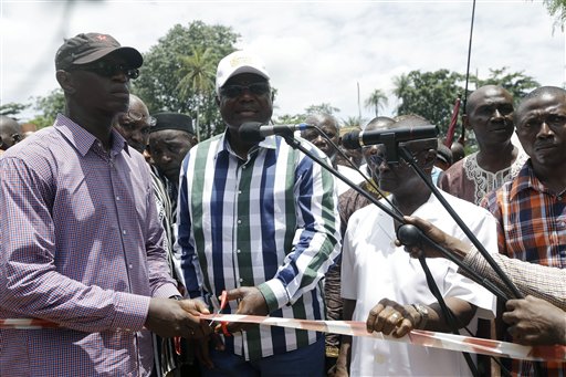 In this photo taken Friday, Aug. 14, 2015, Sierra Leone President Ernest Bai Koroma, centre, cuts a tape to release people from quarantine in the village of Massessehbeh on the outskirts of Freetown, Sierra Leone.  Five months after a man traveled to his home village for festivities marking the end of Ramadan, and died suddenly from Ebola, but now President Koroma came to cut down the fencing to mark the formal end of Sierra Leone's largest remaining Ebola quarantine.  (AP Photo/Sunday Alamba)