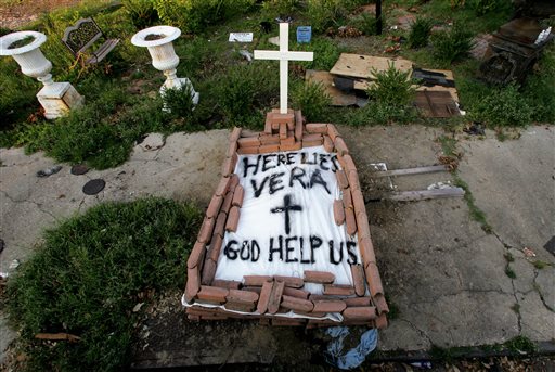 In this Sept. 4, 2005, file photo, a makeshift tomb at a New Orleans street corner conceals a body that had been lying on the sidewalk for days in the wake of Hurricane Katrina. The message reads, "Here lies Vera. God help us." Smiths cremated remains were later reburied in Texas, yet she remains part of her old community. (AP Photo/Dave Martin, File)