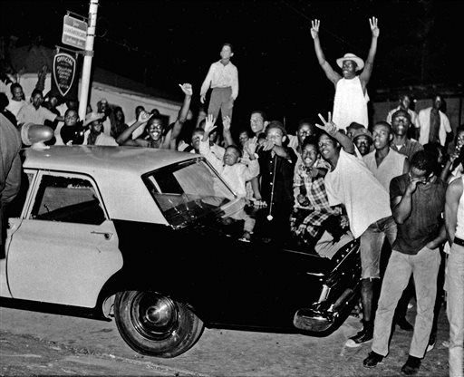 FILE - In this Aug. 12, 1965 file photo, demonstrators push against a police car after rioting erupted in the Watts district of Los Angeles. It began with a routine traffic stop 50 years ago this month, blossomed into a protest with the help of a rumor and escalated into the deadliest and most destructive riot Los Angeles had seen. The Watts riot broke out Aug. 11, 1965 and raged for most of a week. When the smoke cleared, 34 people were dead, more than a 1,000 were injured and some 600 buildings were damaged .(AP Photo, File)