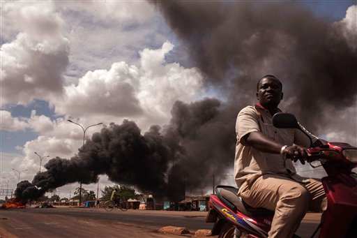 Tires burn, left rear,  as people continue  protesting against the recent coup in  Ouagadougou,  Burkina Faso, Saturday, Sept. 19, 2015.  Senegal President Macky Sall deplored a "lack of dialogue" as mediators entered a second day of talks on Saturday over Burkina Faso's coup in which an elite military unit overthrew the transitional government. (AP Photo/Theo Renaut)