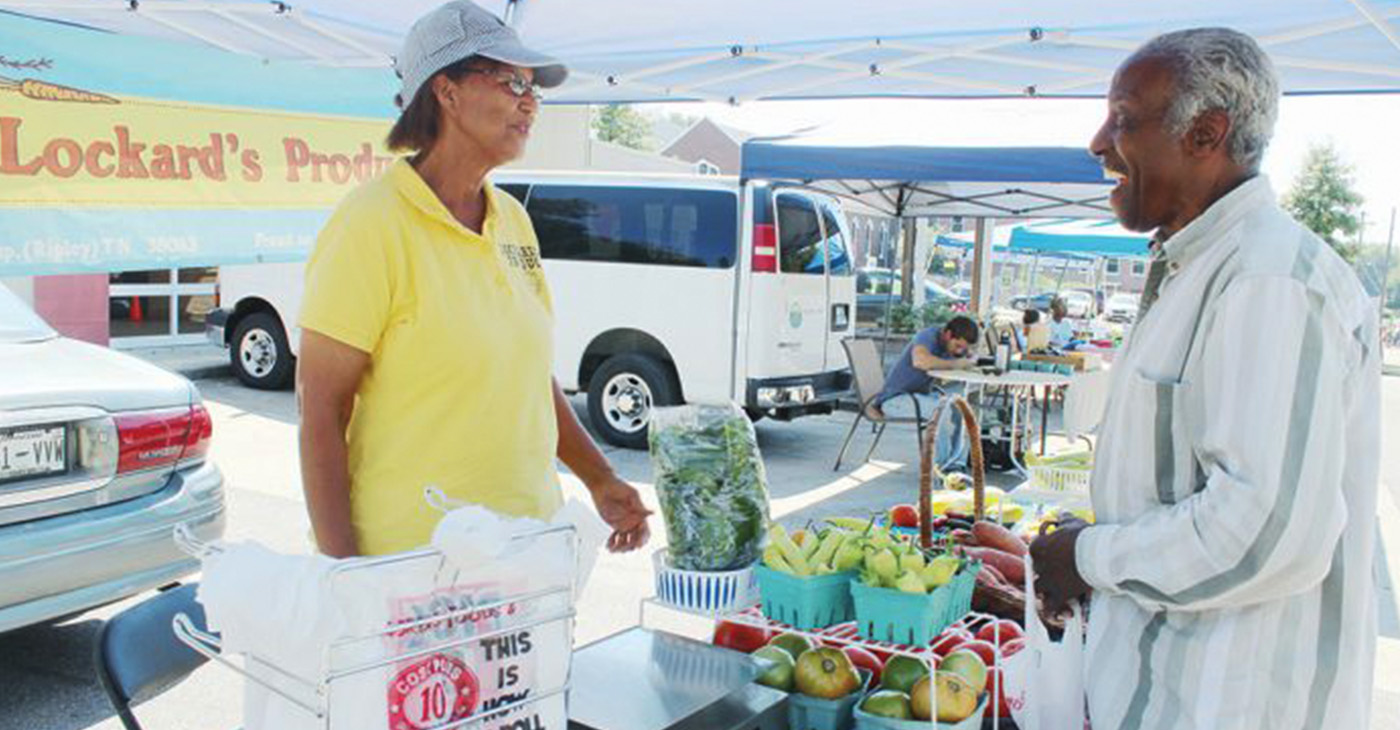 “(Being a farmer) pays off when a customer comes back and tells me how good (my produce) tastes,” said Debra Lockard, shown here talking shop with a patron at the South Memphis Farmers Market in October. (Photo: Lee Eric Smith)