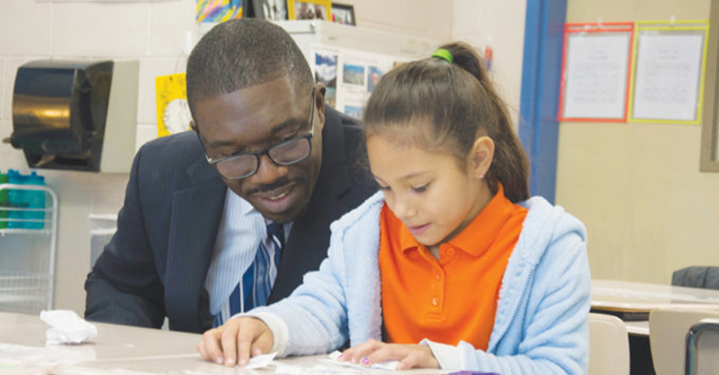 At one of his more than 400 school visits, Dr. Shawn Joseph looks on as an elementary student works on a class project.