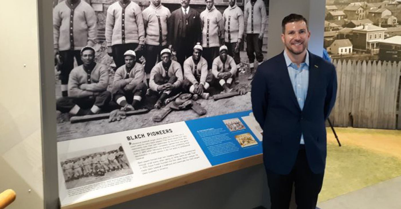 Michael Goldklang standing in front of a museum photo of the St. Paul Colored Gophers team (Photo by: Charles Hallman | MSR News)