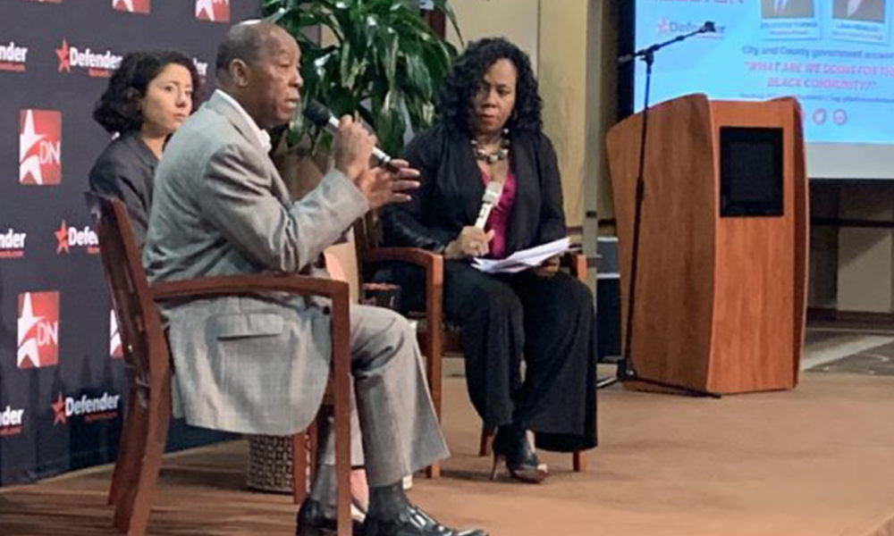 Houston Mayor Sylvester Turner with microphone sitting next to Harris County Judge Lina Hidalgo (Photo by: defendernetwork.com)