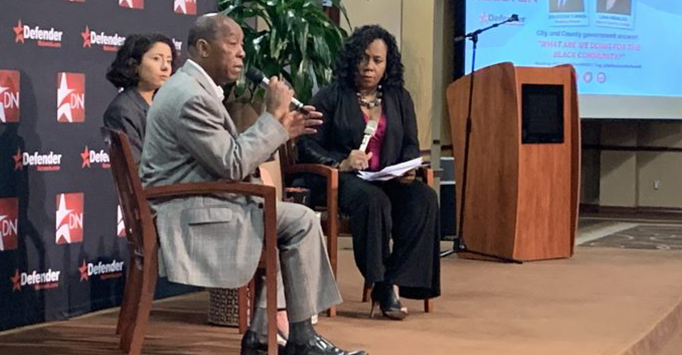 Houston Mayor Sylvester Turner with microphone sitting next to Harris County Judge Lina Hidalgo (Photo by: defendernetwork.com)