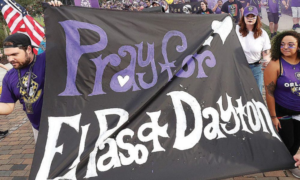 Fans carry a sign that reads, “Pray for El Paso & Dayton” during a march before a pro soccer match in Orlando on Tuesday.