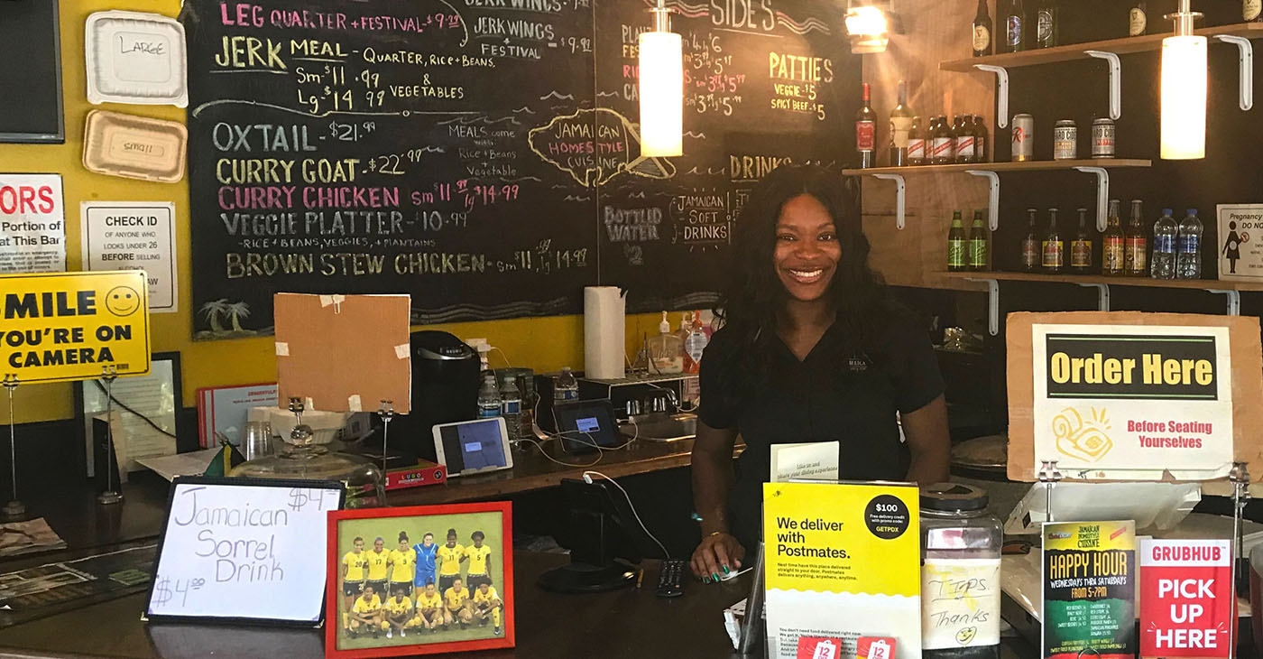 In this photo, Keacean Phillips, owner of Jamaican Homestyle Cuisine, poses behind the register at her restaurant located on North Killingsworth St. in Portland, Ore. (Photo by R. Dallon Adams)