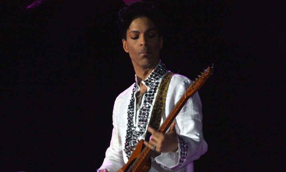 On the title track, Prince sings: “Welcome 2 America, the land of the free – home of the slave.” Prince fans know that track is reminiscent of his 1985 song, “America,” from his “Around the World in a Day” album. (Photo: Prince playing at Cochella, 2008. / Wikimedia Commons)