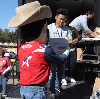 Big Tex shows off the latest Texas Metro News publication while lending a helping hand to volunteers loading a truck delivering food to the surrounding community