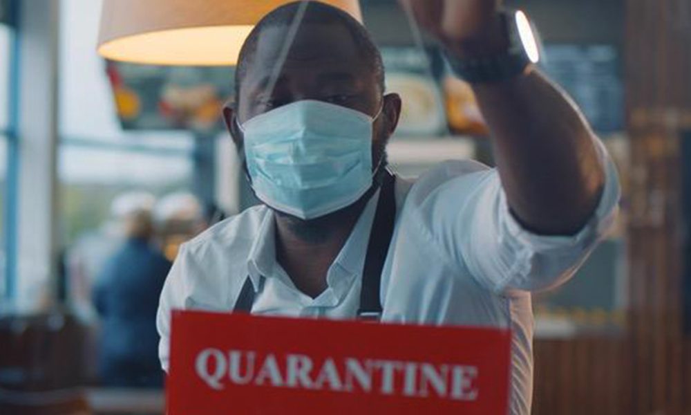 A masked worker stands behind a sign warning of a quarantine. iStock photo.