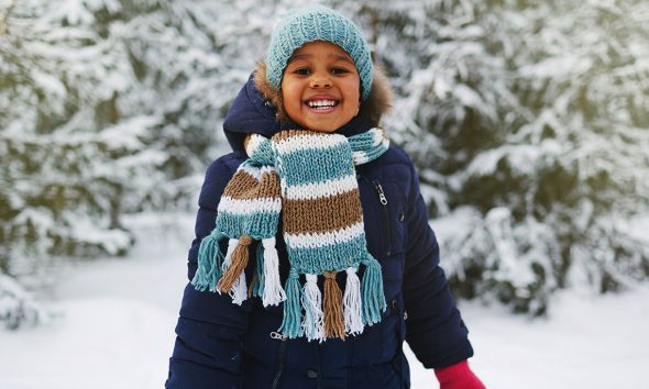 Joyful kid in winterwear looking at camera in natural environment in winter