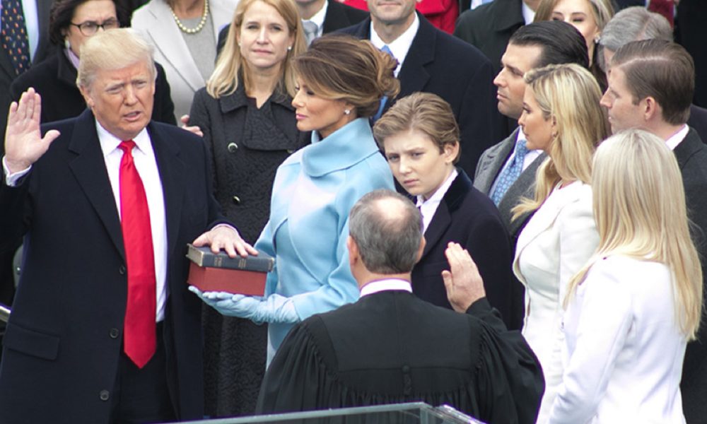 President Donald Trump being sworn in on January 20, 2017 at the U.S. Capitol building in Washington, D.C. Melania Trump wears a sky-blue cashmere Ralph Lauren ensemble. He holds his left hand on two versions of the Bible, one childhood Bible given to him by his mother, along with Abraham Lincoln’s Bible. Photo: Official White House Facebook page. Facebook.