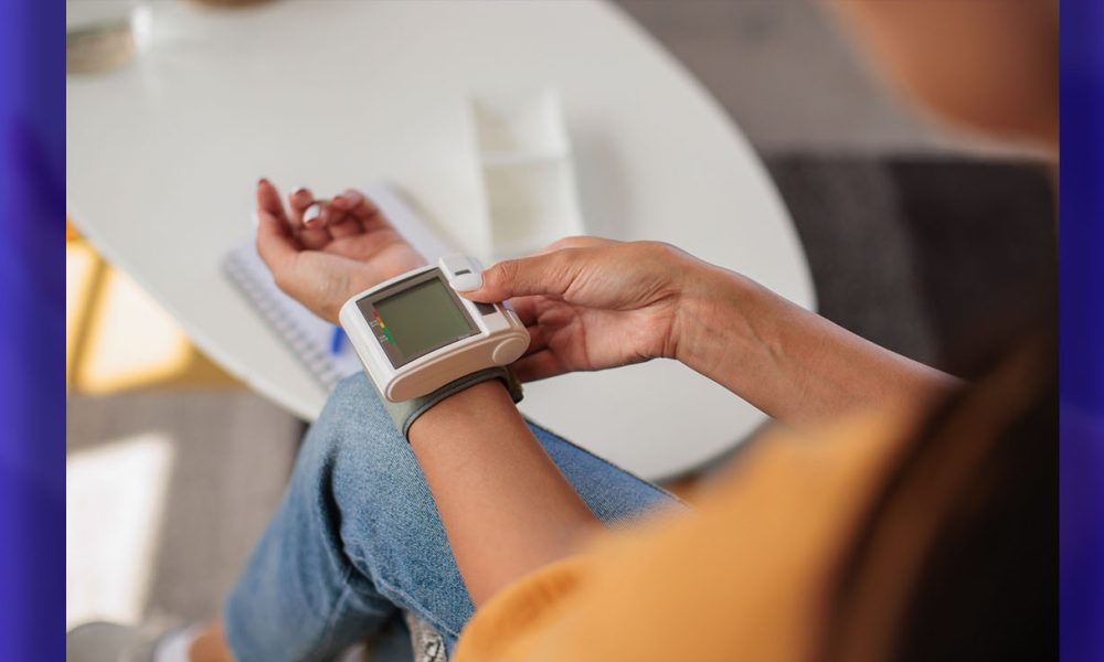 Unrecognizable woman measures her blood pressure using a wrist monitor in her cozy living room.