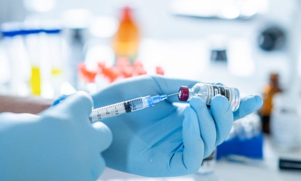 A concept photo of a scientist's hand holding a bottle of the COVID-19 vaccine and measuring the right amount of dosage.