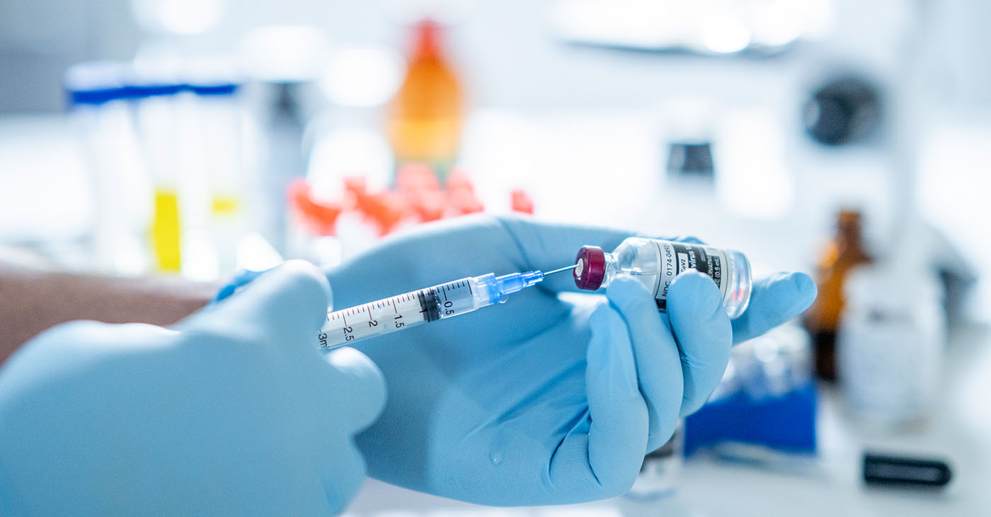 A concept photo of a scientist's hand holding a bottle of the COVID-19 vaccine and measuring the right amount of dosage.