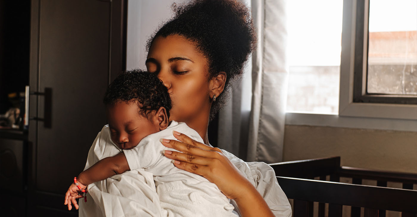 Young adult mother holding and kissing her newborn. (Photo by Djavan Ridriguez)