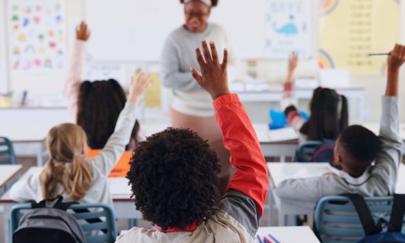 Children, back and hands raised at school with for question, answer and learning at youth academy. Kids, education and teacher for development with sign for talking, quiz and scholarship in classroom (Photo b Jacob Wackerhausen)