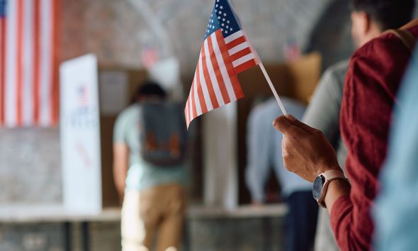 Close up of African American voter with national flag in waiting line during US elections. (Photo by Drazen Zigic)