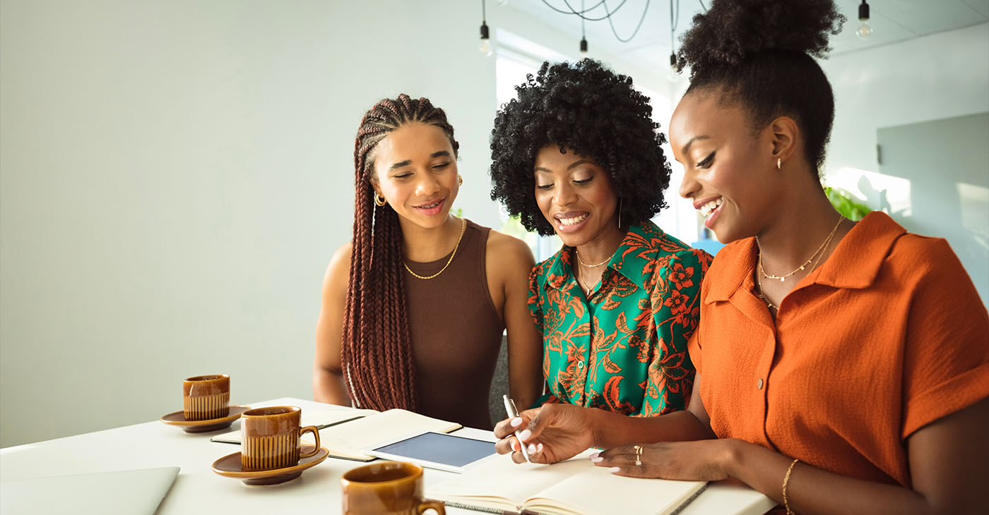 Teamwork concept. Three beautiful black women wearing dresses sitting at the table in an office and discussing over project.