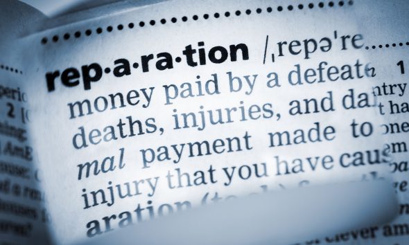 The Dictionary definition of the word “reparation” photo taken through magnifying glass from a page of a dictionary with selective focus.