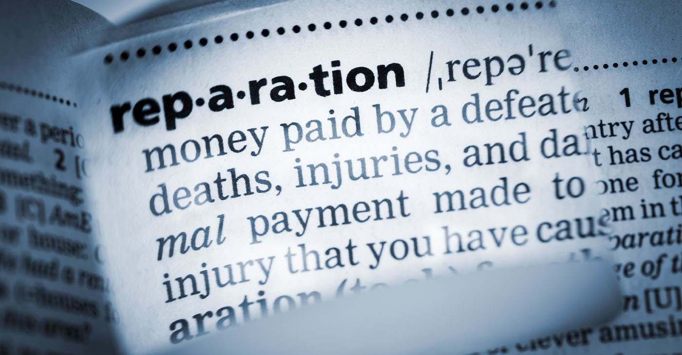 The Dictionary definition of the word “reparation” photo taken through magnifying glass from a page of a dictionary with selective focus.