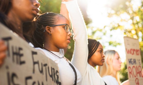 Diverse group of teenage girls holding hands in unity and holding up protest signs during a women's rights march (Photo by Nicky Lloyd)
