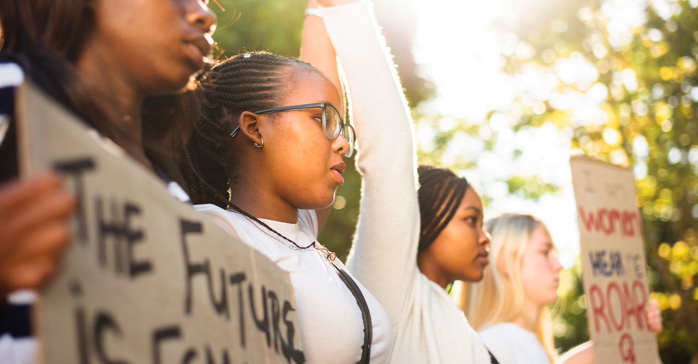 Diverse group of teenage girls holding hands in unity and holding up protest signs during a women's rights march (Photo by Nicky Lloyd)